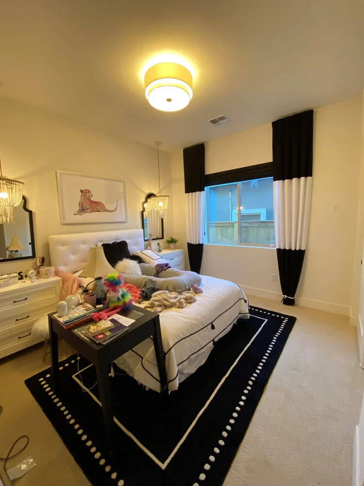 Cozy bedroom with white bed, black and white rug, black and white curtains, and bedside tables with lamps.