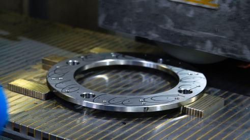 Pièce métallique circulaire usinée avec des motifs gravés, posée sur une table en métal d'une machine industrielle.