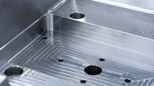 Surface métallique usinée avec plusieurs trous de différentes tailles et rainures linéaires.