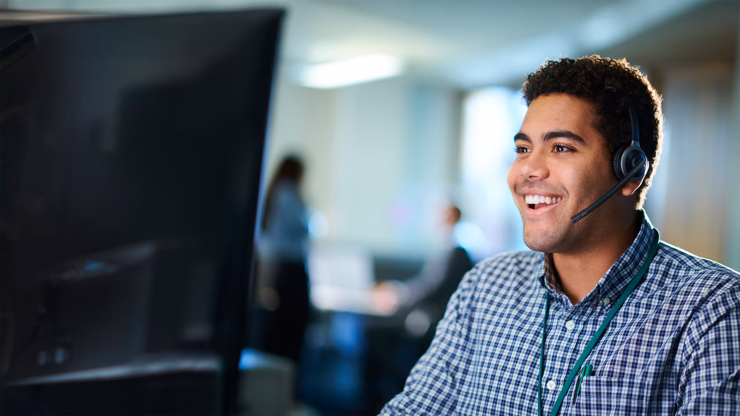 Customer Service Advisor wearing a headset and checkered shirt working at a computer in an office.