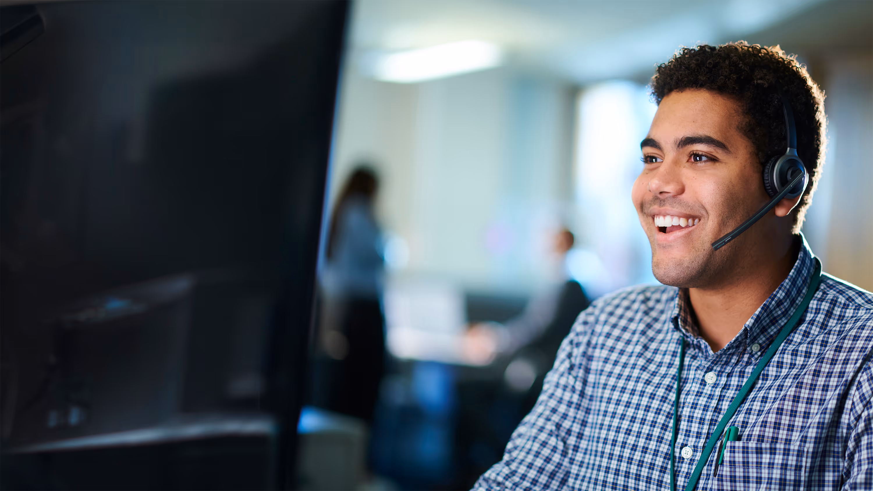 Customer Service Advisor wearing a headset and checkered shirt working at a computer in an office.