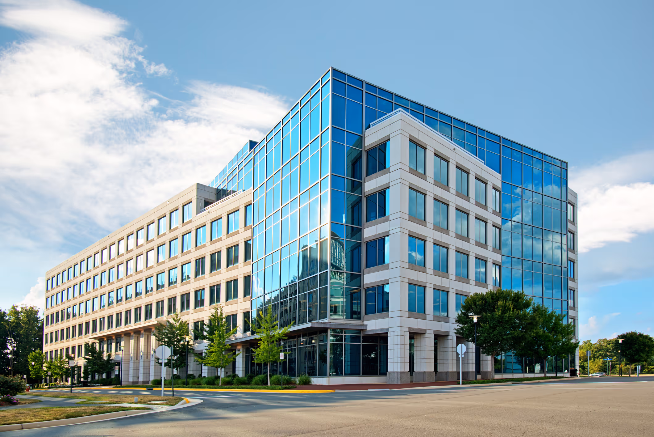 Modern office building with large reflective glass windows and blue sky with clouds.