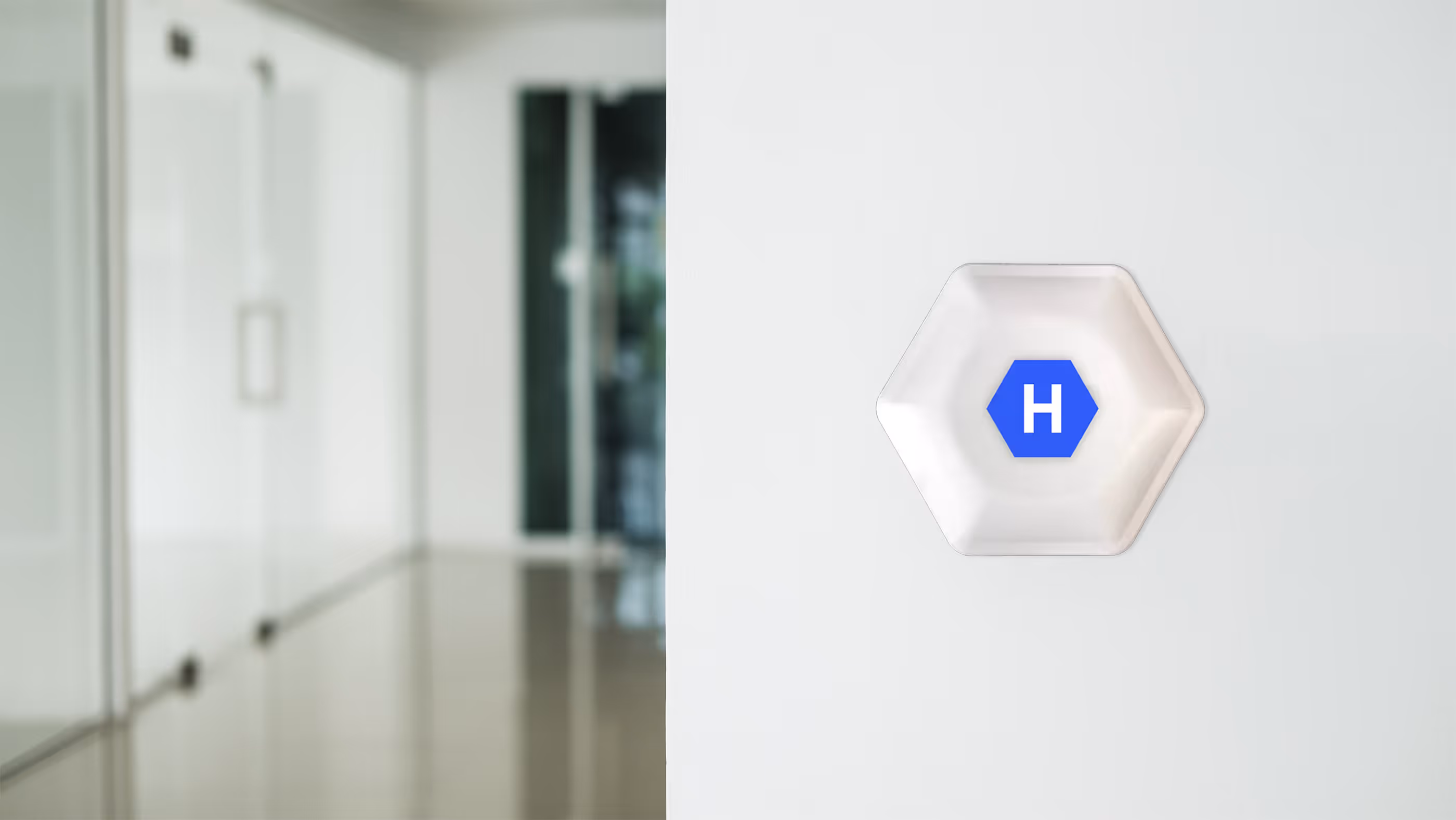 White hexagonal device with a blue hexagon and white letter H mounted on a white wall in a modern office setting.