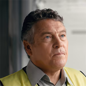 Middle-aged man wearing a yellow safety vest and gray shirt, looking slightly upward.