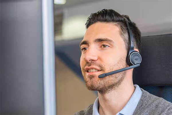 Man with dark hair and beard wearing a headset and looking at a computer screen.