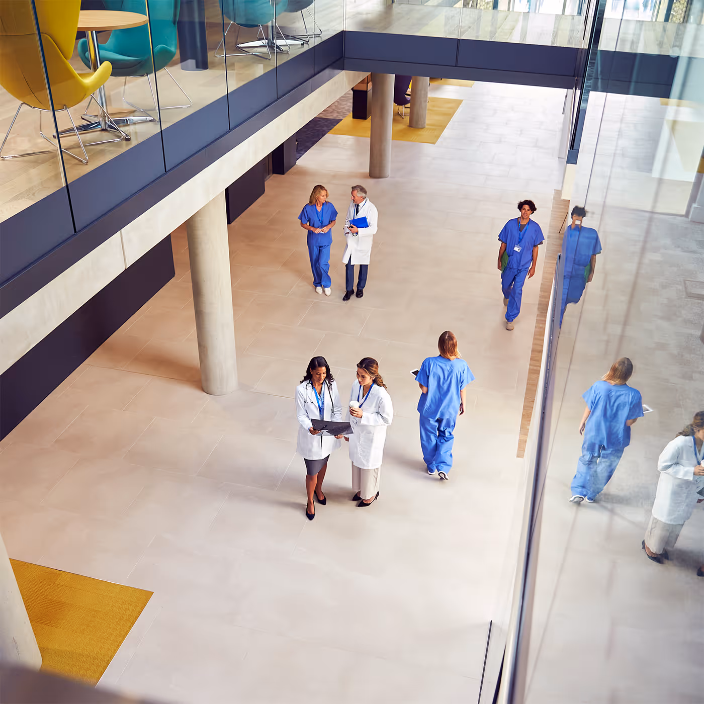 Doctors and nurses walking and talking in a modern hospital lobby with glass walls and natural light.