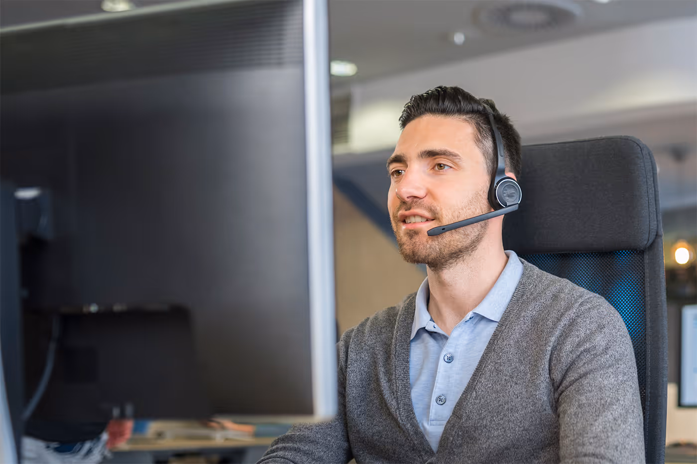 Man wearing headset working at a computer in an office setting.
