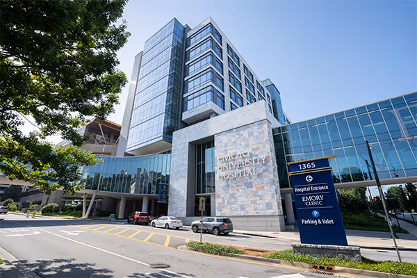 Exterior view of Emory University Hospital building with adjacent skybridge and signage for hospital entrance and parking.