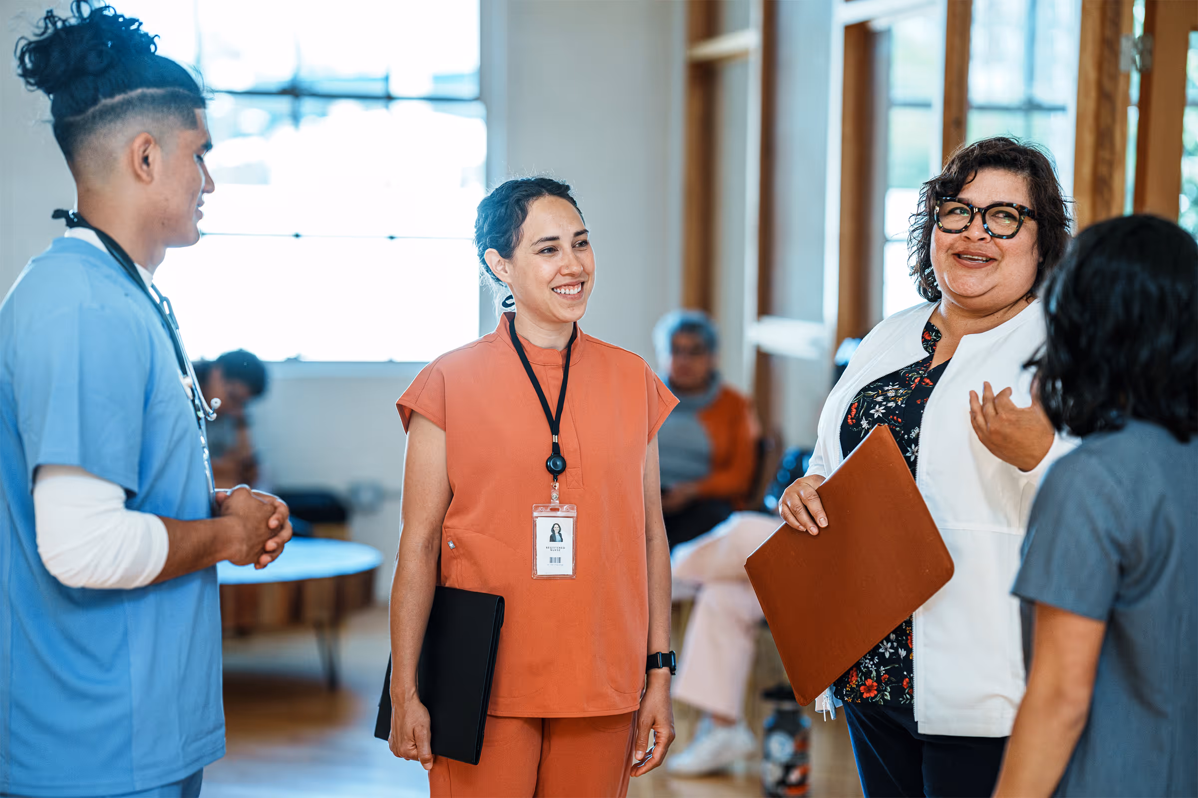 Healthcare professionals in scrubs and a white coat engaged in a friendly conversation inside a medical facility.