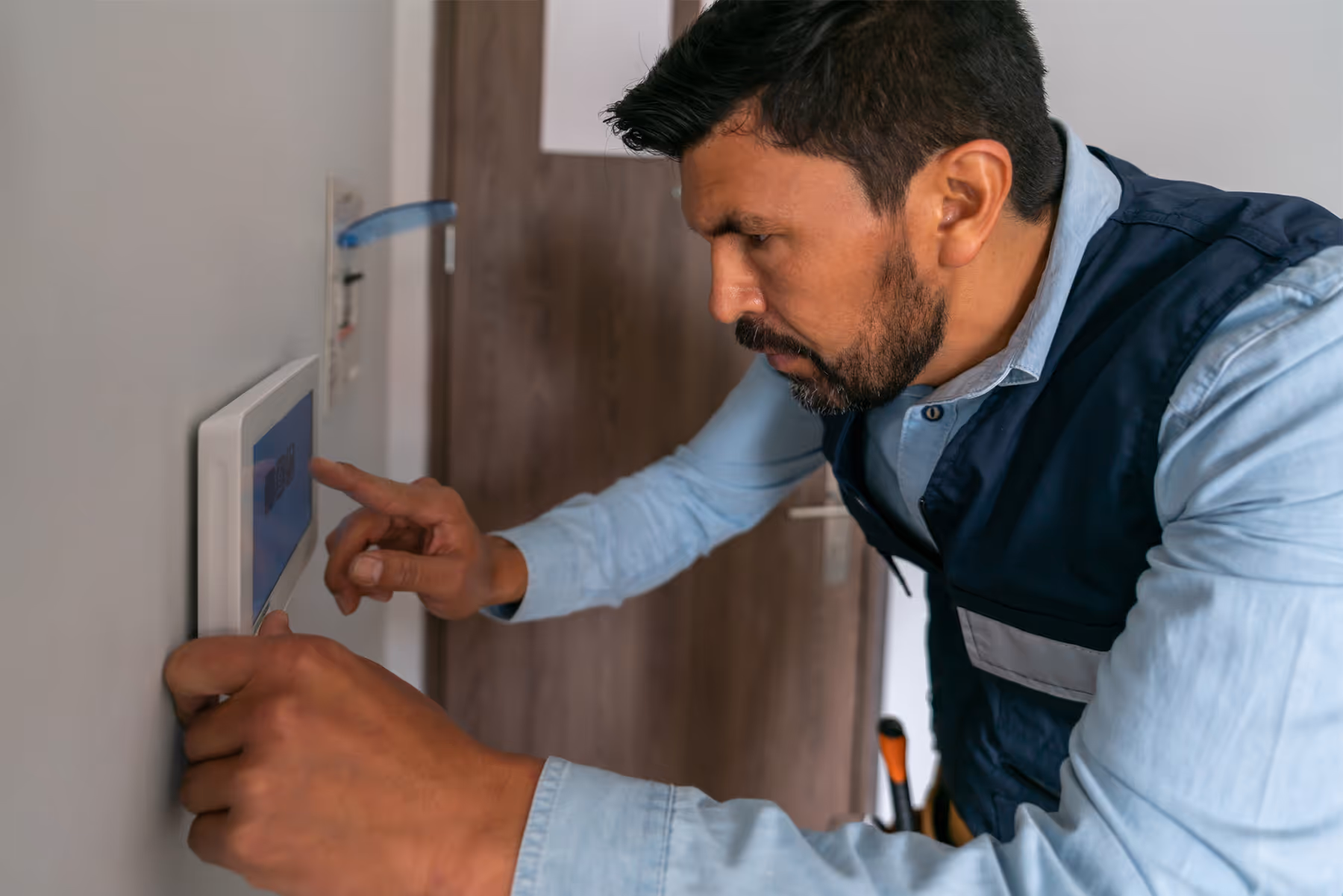 Man adjusting a wall-mounted digital thermostat in a home interior.