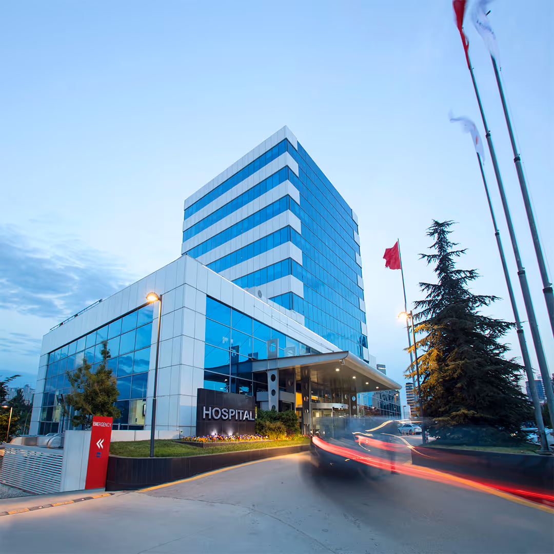 Modern hospital building with glass windows and car driving past main entrance at dusk.