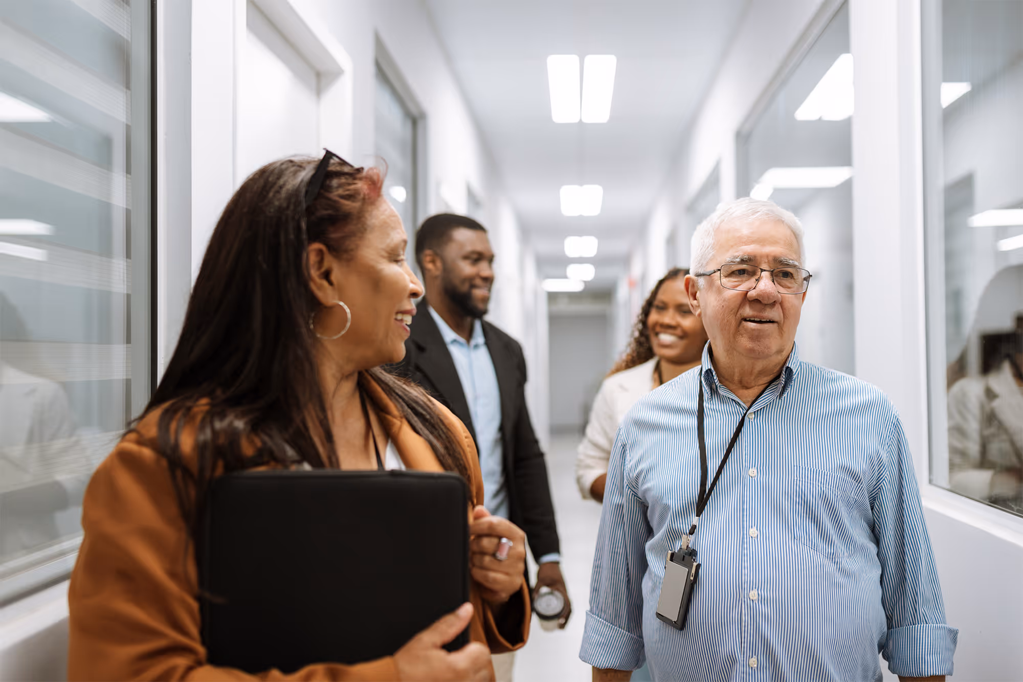 Four diverse colleagues smiling and walking together in a bright office hallway.
