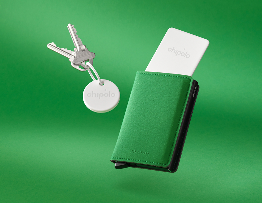 Two silver keys attached to a white Chipolo key finder, next to a green and black Secrid wallet with a white Chipolo card partially inserted.