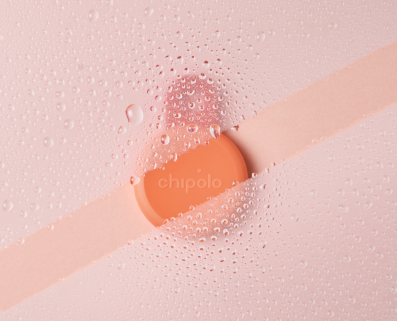Orange Chipolo tracker on a pink surface with water droplets on a glass overlay.