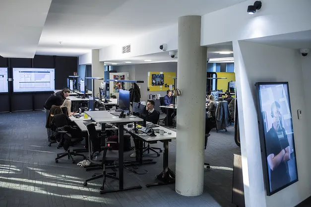 Moderne Bürofläche mit Mitarbeitern, Computern und Schreibtischen in hellem, offener Raum.