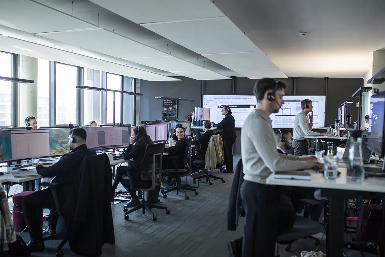 Team arbeitet an Schreibtischen mit Headsets in einem modernen, hellen Büro.