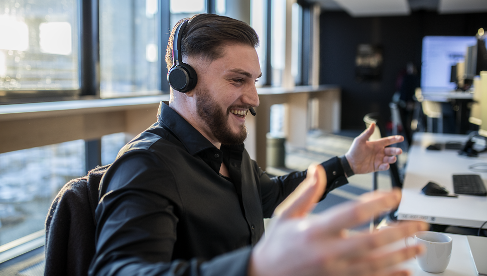 Mann mit Headset spricht und gestikuliert begeistert in einem hellen Büro.