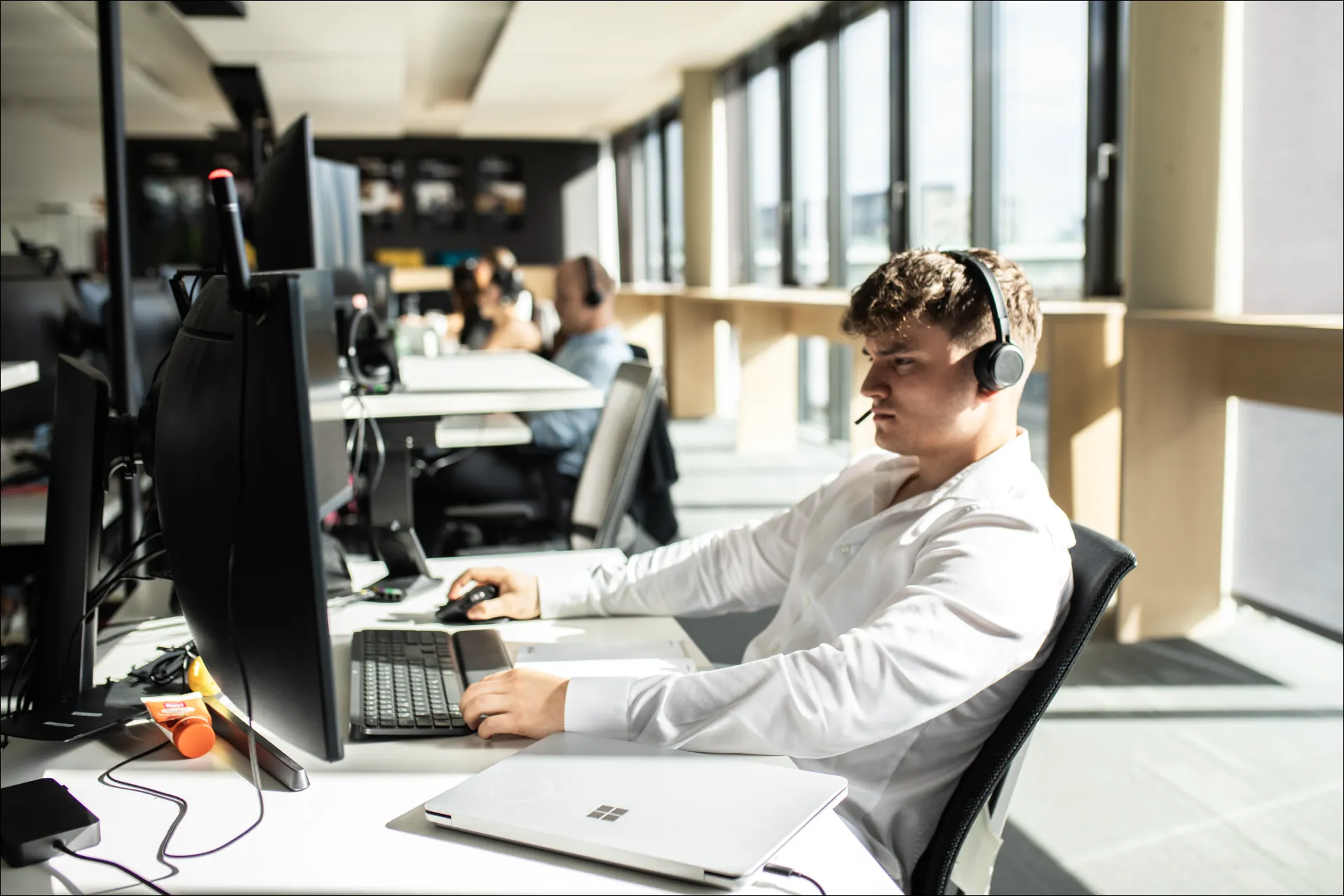 Mann mit Headset arbeitet konzentriert an Schreibtisch mit mehreren Bildschirmen im Büro