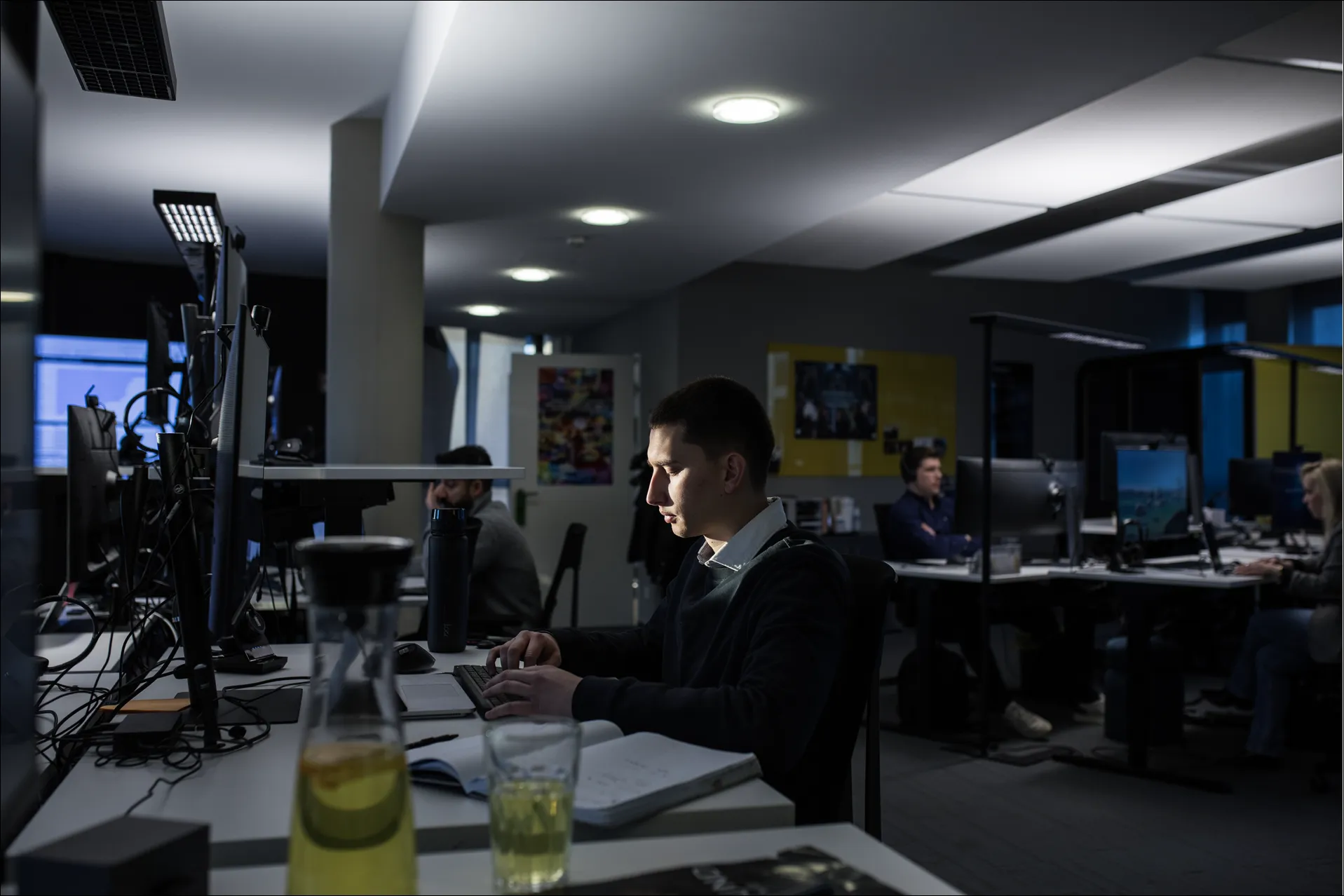 Junger Mann arbeitet konzentriert spät abends an Computer in einem dunklen, modernen Büro.