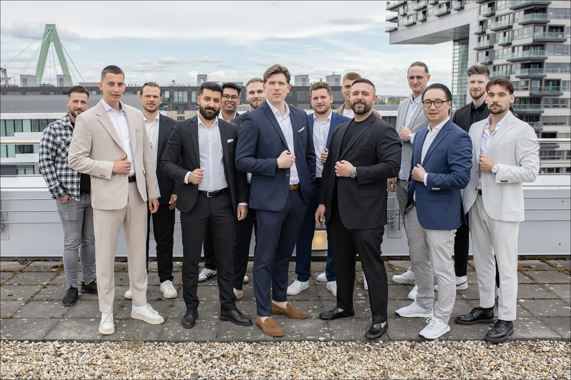 Gruppe von Männern in Anzügen steht selbstbewusst auf einer Dachterrasse vor moderner Stadtarchitektur.