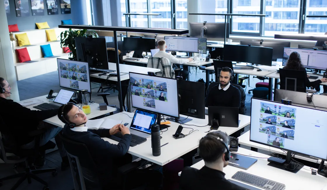 Moderne Büroumgebung mit mehreren Mitarbeitern, die Kopfhörer tragen und an Computern arbeiten.