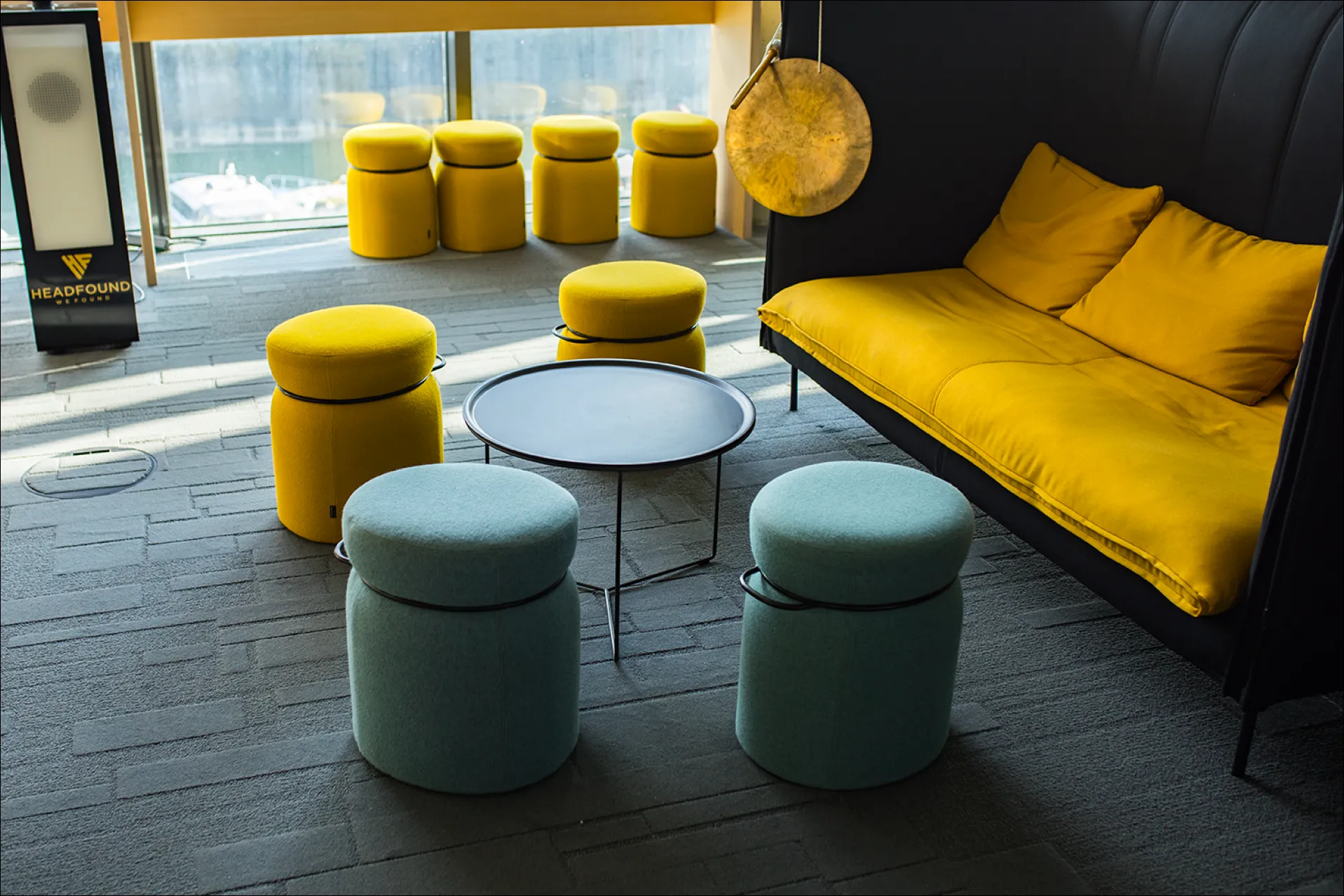 Gelbe und blaue gepolsterte Hocker um runden schwarzen Tisch neben gelbem Sofa im modernen Raum.