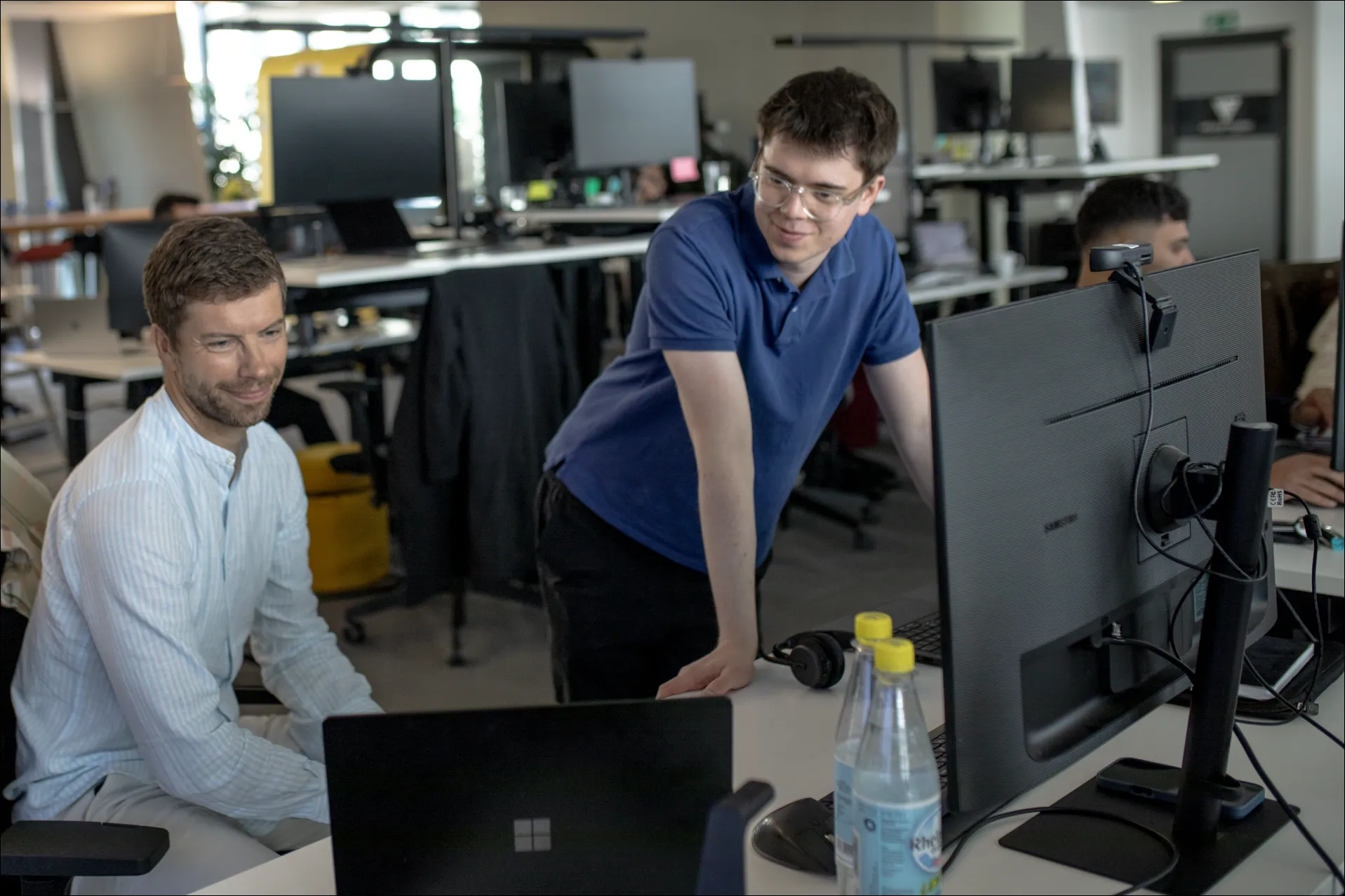 Mehrere Personen arbeiten an Computern in einem modernen Büro mit großen Fenstern.