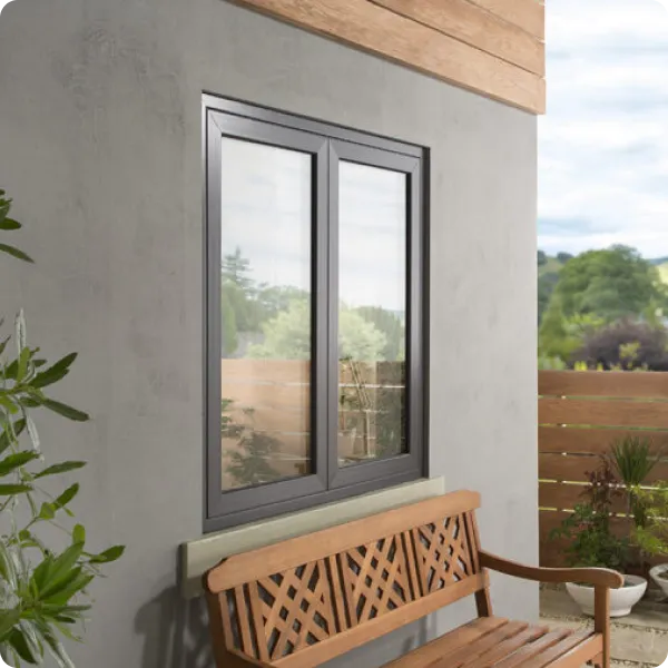 Modern dark gray two-panel flush sash window on a gray exterior wall above a wooden bench, with plants nearby and a wooden fence in the background.