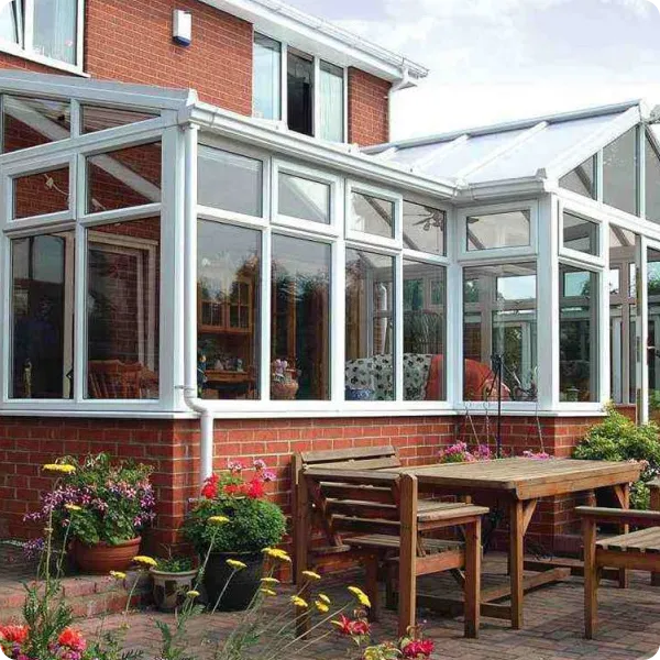 Wooden outdoor dining set with benches and table on patio next to a brick house with a white glass conservatory.