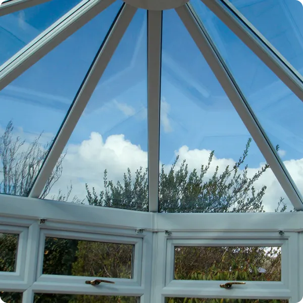 View through a glass conservatory roof with blue sky and clouds visible above trees outside.