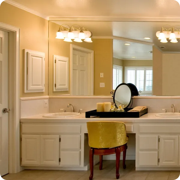 Bathroom vanity with large mirror, dual sinks, a tray holding a round mirror and candles, and a yellow upholstered chair.
