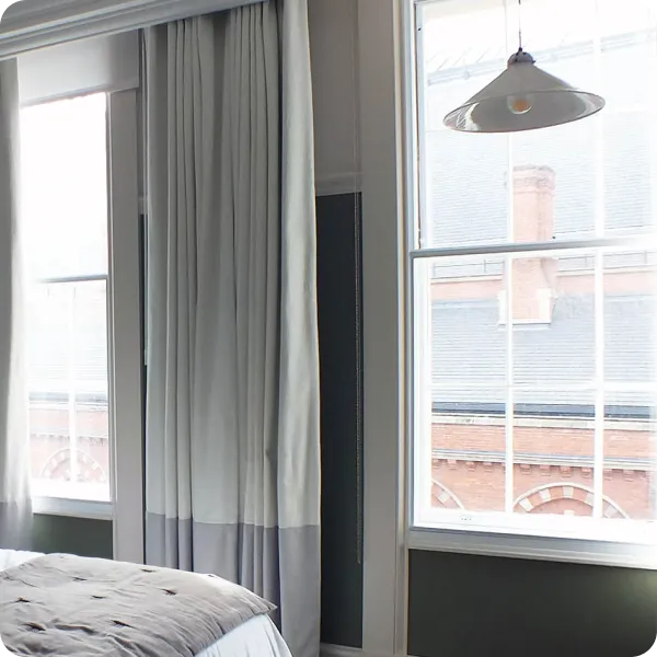 Bedroom window with sheer white curtains and a pendant light above a partially visible bed.