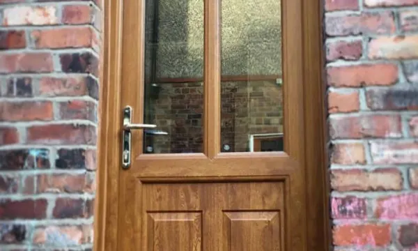 Wooden front door with glass panels set in a brick wall with a metal handle and lock.