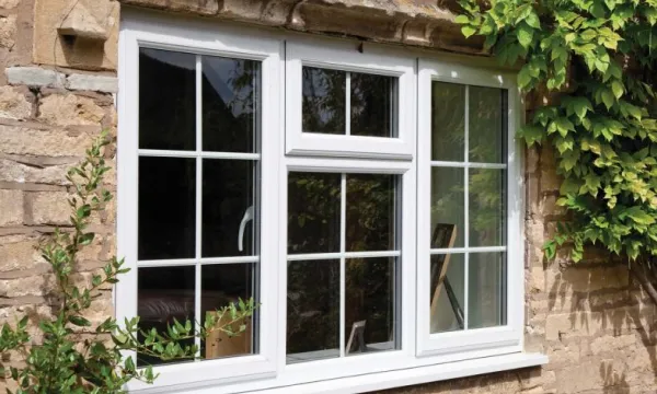 White-framed three-section window with glass panes set in a stone wall covered with green ivy on the right side.