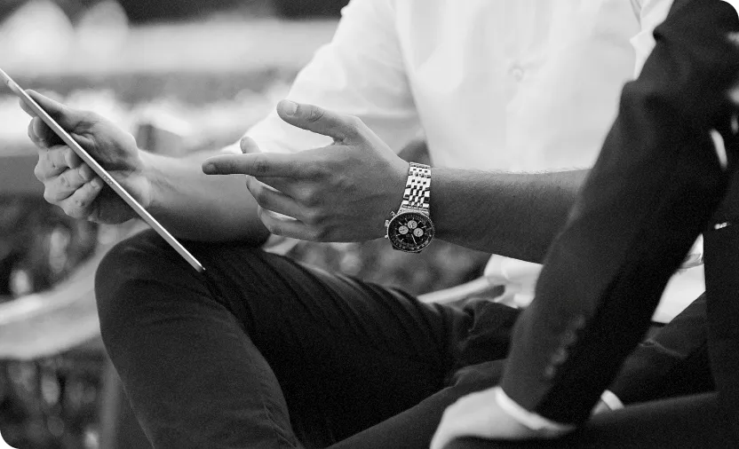 Black and white photo of a person in a white shirt showing a tablet to another person in a suit during a discussion.