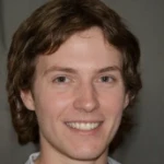 Young man with light skin, brown hair, and a friendly smile against a dark background.