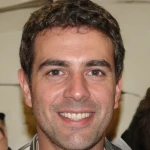 Portrait of a smiling man with short curly dark hair and brown eyes.