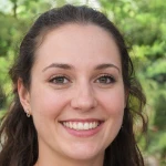 Smiling young woman with dark hair and green eyes outdoors with blurred greenery background.