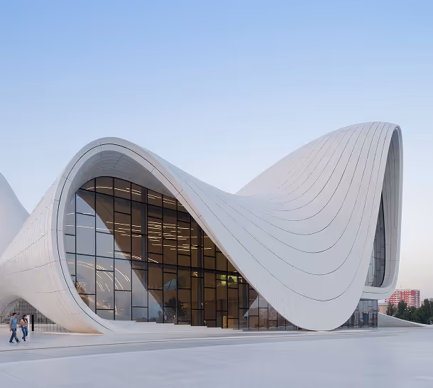 Modern white curvilinear building with large glass windows and a smooth wave-like roof design under a clear sky.