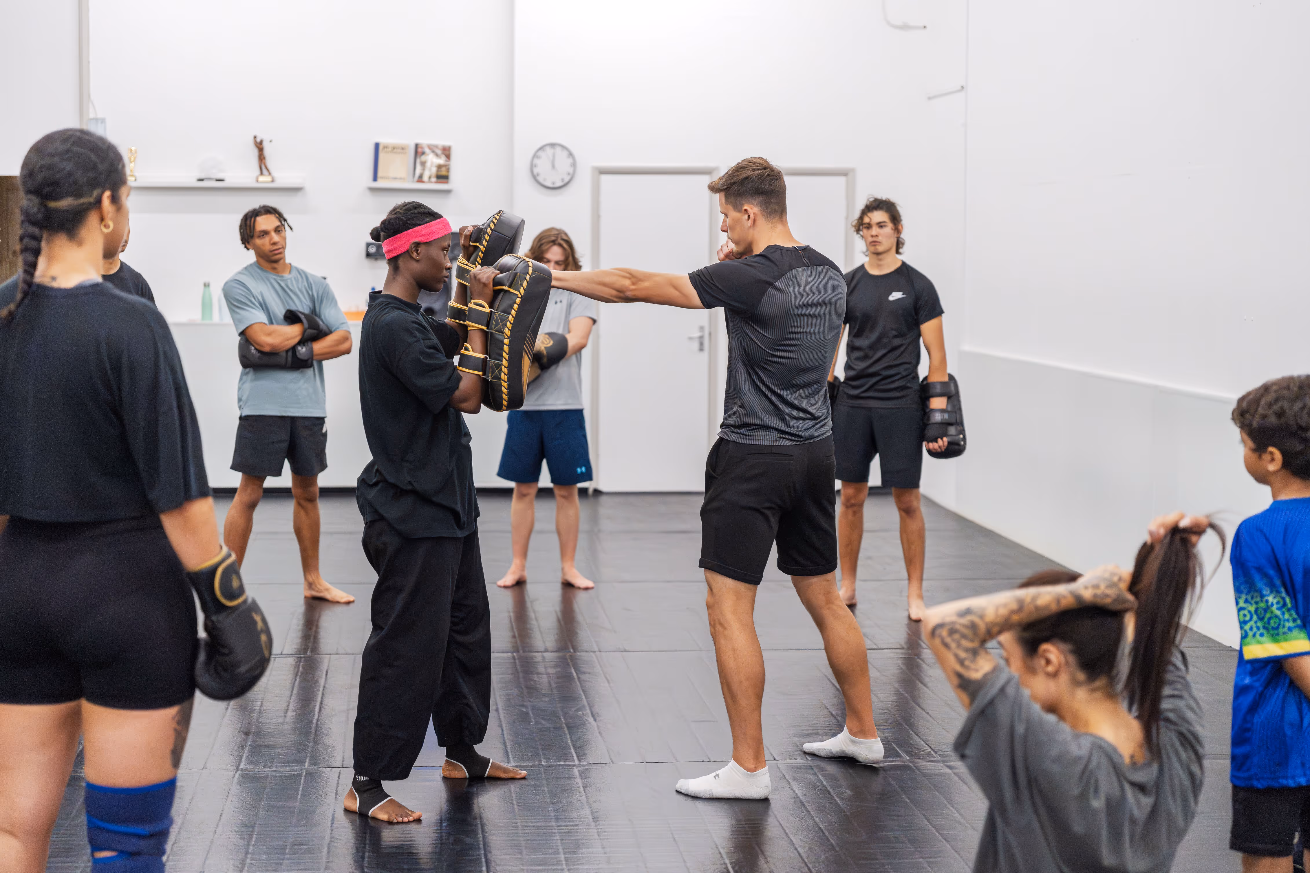 Group of people practicing martial arts in a gym with one man punching pads held by an instructor.