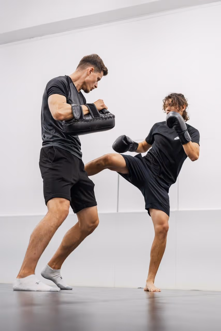 Two men training in kickboxing, one kicking and the other holding pads.