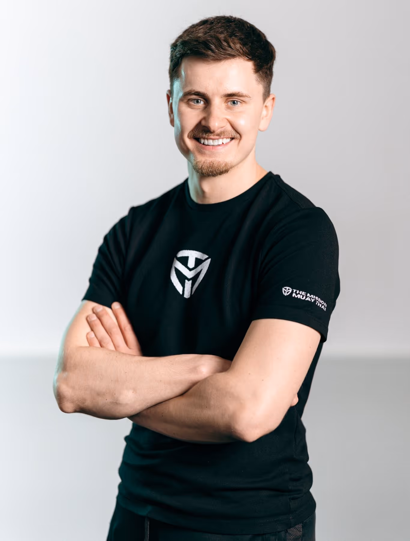 Smiling man in a black T-shirt with crossed arms against a plain light background.