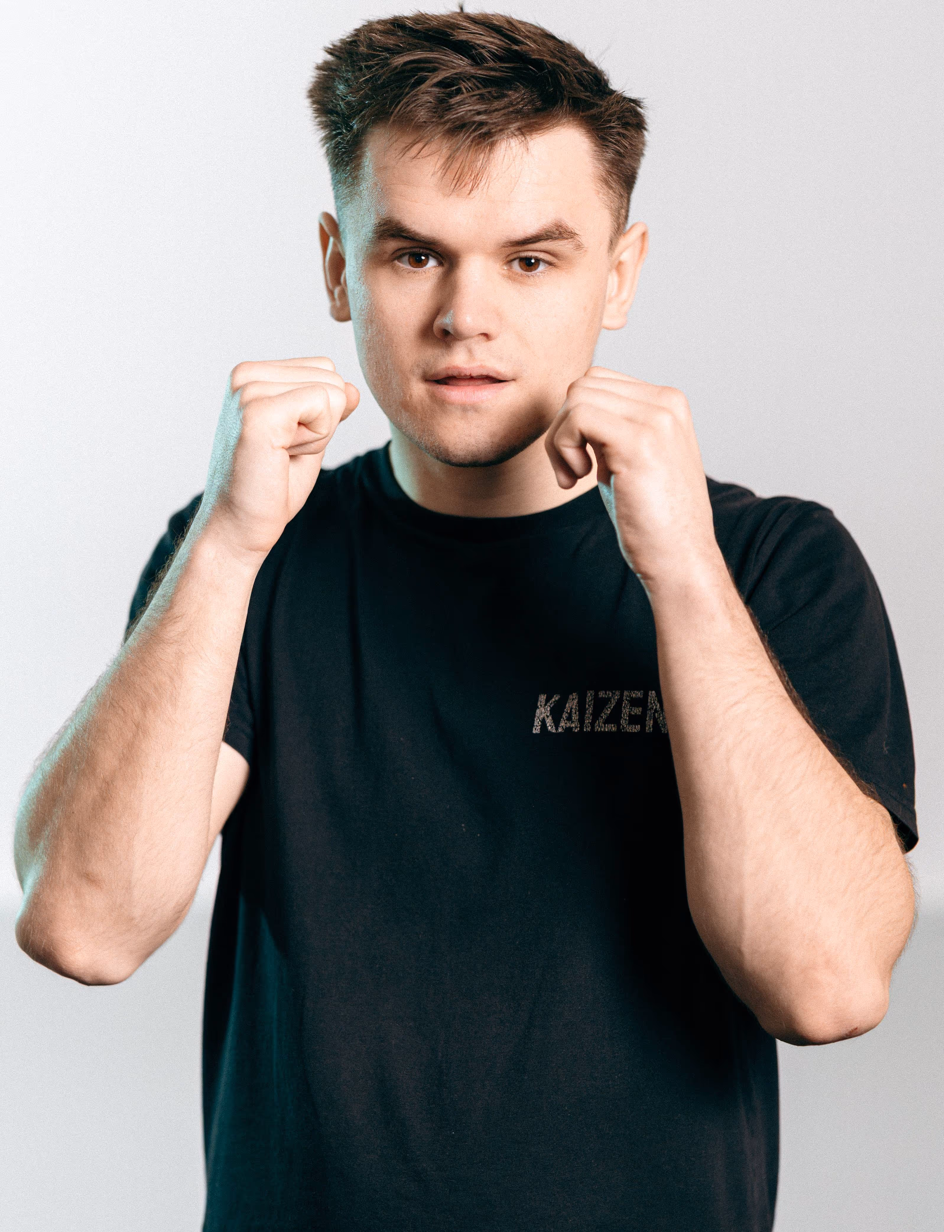Young man with short hair in black Kaizen t-shirt holding fists up in fighting stance.