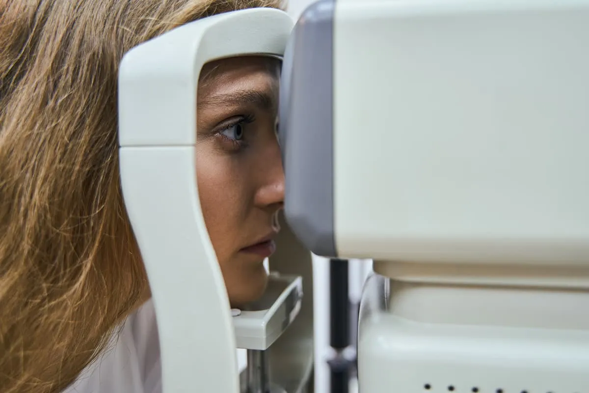 Woman undergoing an OCT eye scan with her chin resting on a white medical device.