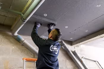 Worker installing insulation panels on a ceiling in an industrial building.