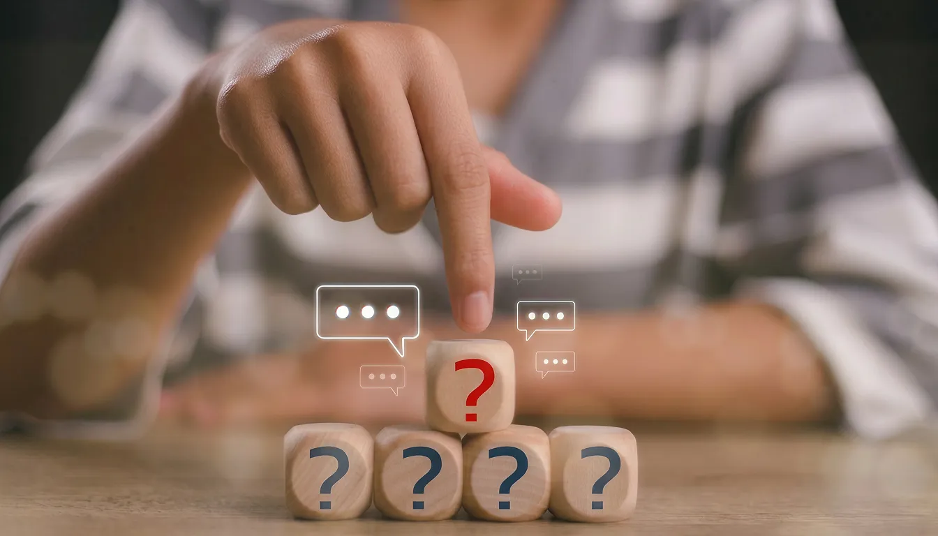 Person pointing at a wooden block with a red question mark, stacked above four blocks with blue question marks and floating chat icons nearby.