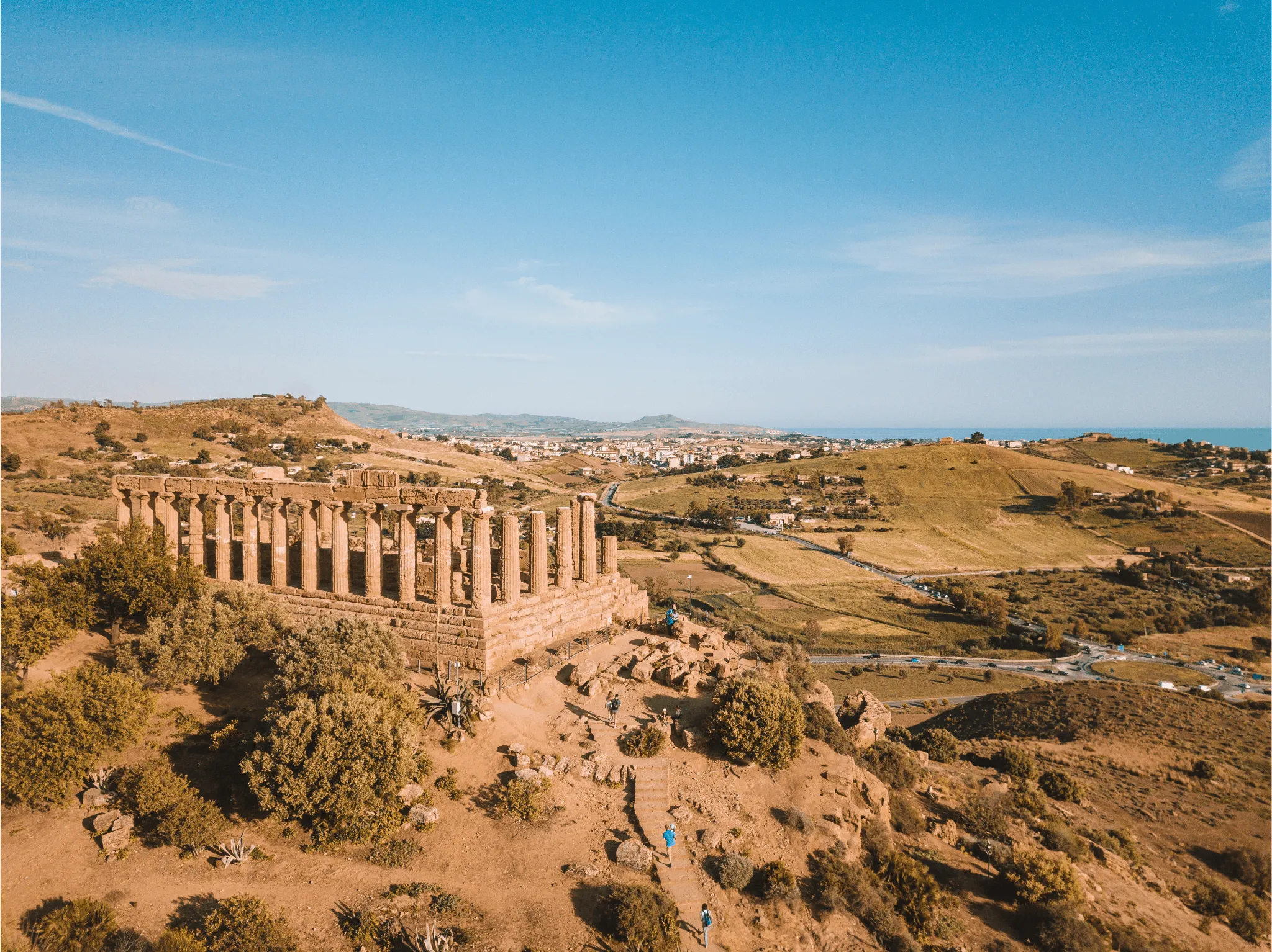 Ancient Greek temple ruins on a hill overlooking a rural landscape under a clear blue sky.