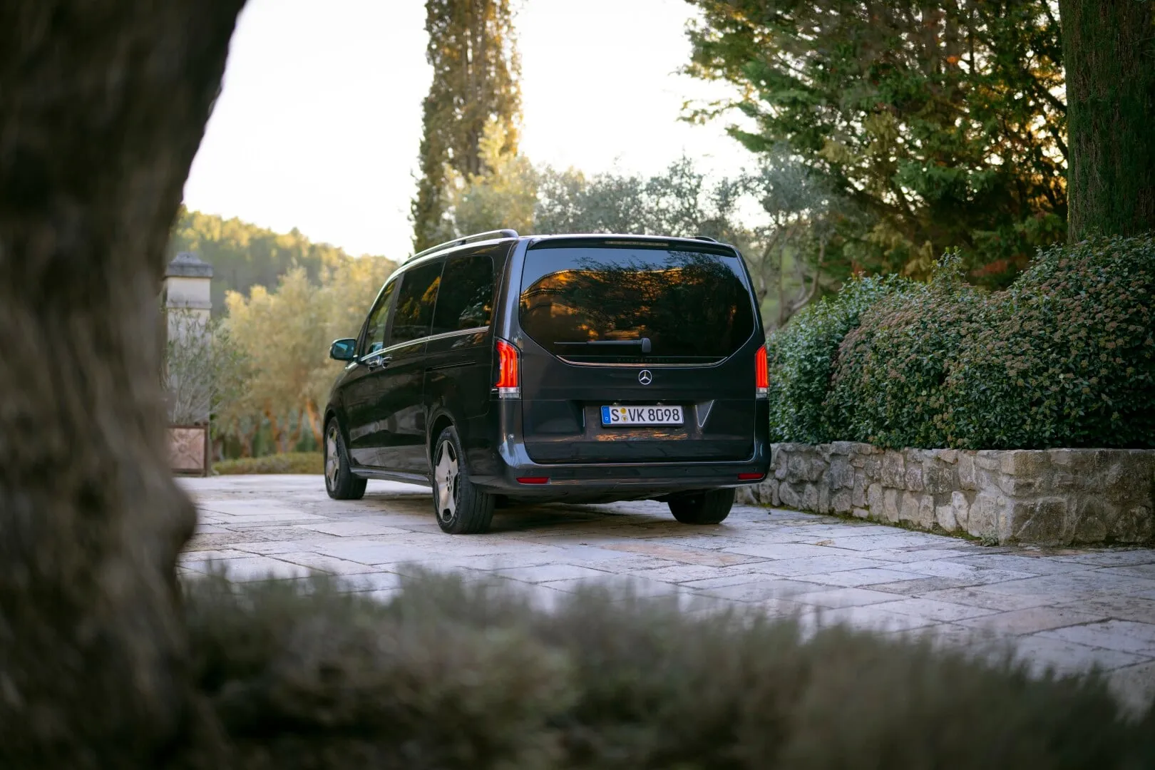 Black Mercedes-Benz van parked on a stone driveway with greenery and trees around.