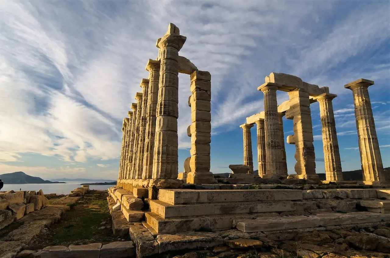 Ancient stone ruins of a Greek temple with columns under a partly cloudy sky at sunset.