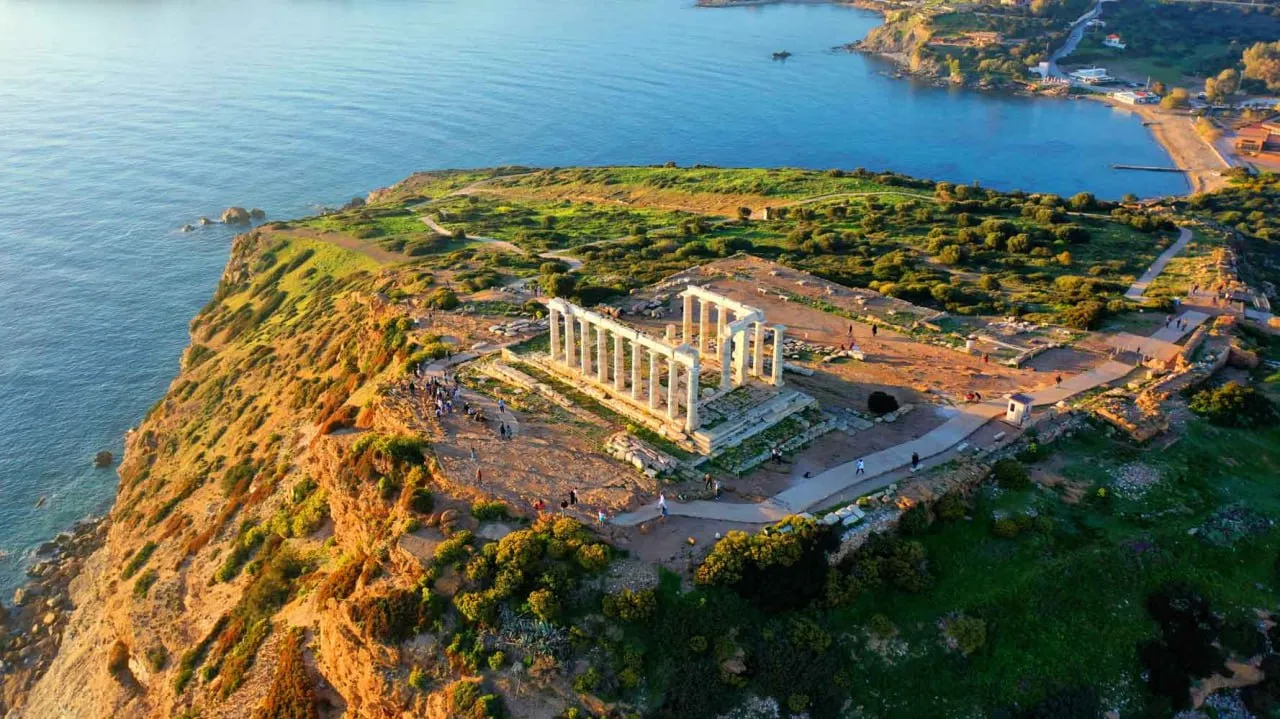 Aerial view of ancient temple ruins on a cliff overlooking the sea at sunset.